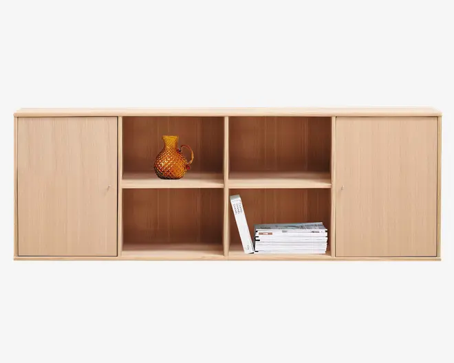 Rektangulær reol i lyst træ med glat overflade. Den har to lukkede rum med låger i hver ende og fire åbne hylder i midten. På de åbne hylder står en ravfarvet glaskande med struktur samt en stak bøger og magasiner. Designet er minimalistisk og funktionelt, velegnet til opbevaring og udstilling.