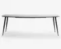 Et moderne bord med en slank, rektangulær hvid bordplade med let afrundede kanter. Bordet understøttes af fire slanke, skråtstillede sorte metalben, hvilket giver det et minimalistisk og nutidigt udseende. Benene er let udadgående for ekstra stabilitet og stil.