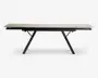 Rektangulært bord med en lys, glat bordplade og sorte, skråtstillede metalben. Bordet har et moderne, minimalistisk design og ser ud til at være udtrækkeligt, hvilket ses på de synlige samlinger og udtræksmekanismen under bordpladen.