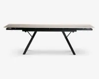 Rektangulært bord med en lys, glat bordplade og sorte, skråtstillede metalben. Bordet har et moderne, minimalistisk design og ser ud til at være udtrækkeligt, hvilket ses på de synlige samlinger og udtræksmekanismen under bordpladen.