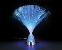 En dekorativ lampe med en sølvfarvet fod fyldt med glimmer og et bundt fine, fleksible fiberoptiske tråde, der spreder sig udad. Trådene udsender et blåt, blødt lys, som skaber en glitrende, stjerneagtig effekt. Lampen har en synlig ledning og er designet til at give stemningsbelysning og et iøjnefaldende visuelt udtryk.