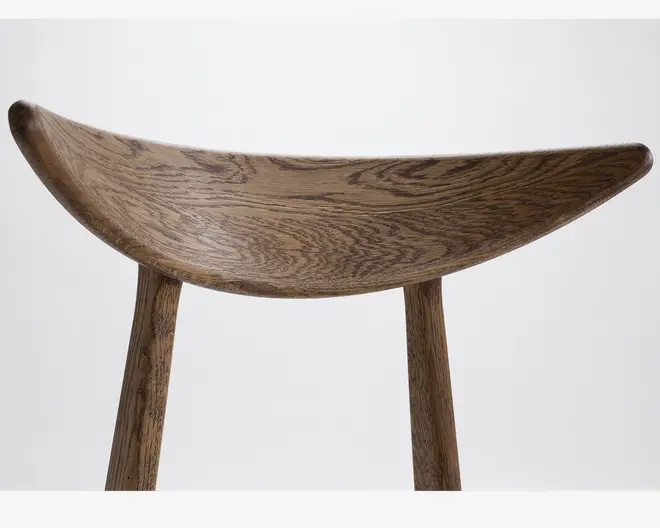 Buet træsæde med en glat, naturlig årestruktur og en sadelformet udformning. Sædet understøttes af to solide, afrundede træben, hvilket giver et minimalistisk og elegant udtryk. Træet har en mellembrun finish, der fremhæver teksturen og de unikke åretegninger.