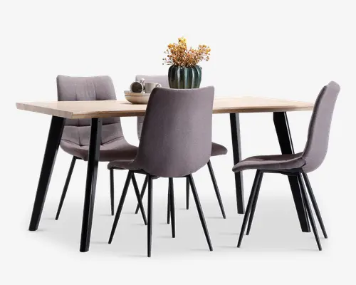 Et rektangulært spisebord i lyst træ med skråtstillede sorte metalben, omgivet af fire polstrede grå stole med slanke sorte ben og en dekorativ vase med tørrede blomster midt på bordet.