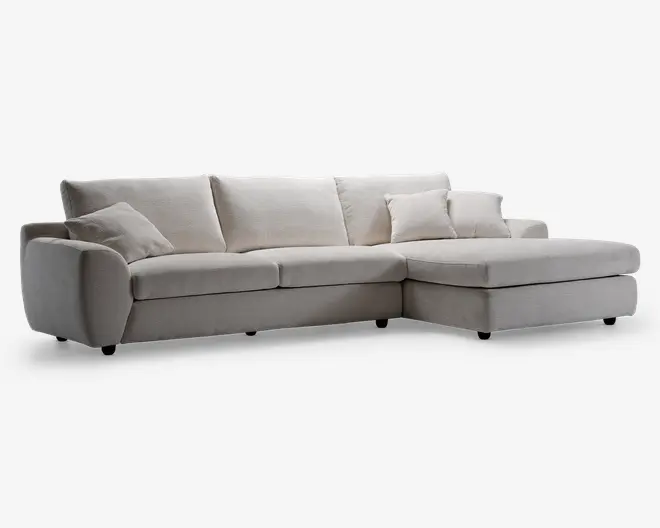 Moderne L-formet hjørnesofa med chaiselong til højre, betrukket med lysebeige stof. Sofaen har brede, afrundede armlæn, tre store ryghynder og tre matchende pyntepuder for ekstra komfort. Sædehynderne er tykke og bløde, hvilket giver en behagelig siddeoplevelse. Designet er minimalistisk og passer godt til moderne stuer.
