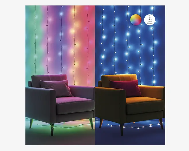 Billedet viser to lænestole placeret side om side foran en væg dekoreret med lodrette rækker af lyskæder. Venstre side har flerfarvede lys i grønne, blå, pink og gule nuancer, hvilket skaber en livlig og farverig stemning. Højre side viser kølige hvide lys mod en blå baggrund, hvilket giver et roligt og moderne udtryk. Begge lænestole har en pude, og belysningen fremhæver forskellen mellem farverig og hvid belysning, hvilket antyder mulighed for tilpasning af lyset.