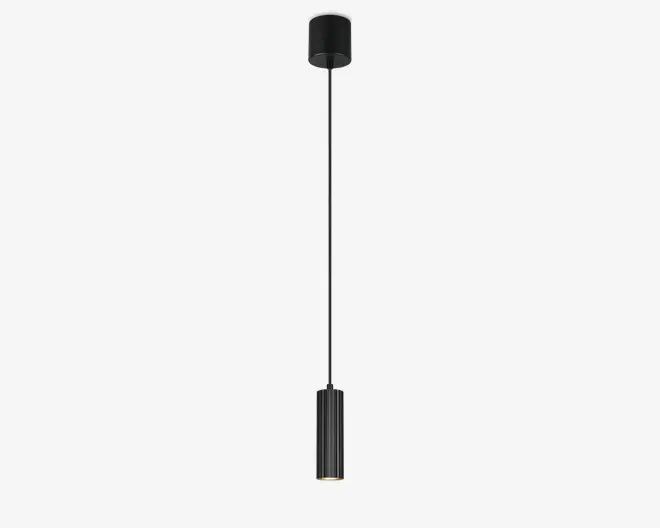 Slank, cylindrisk pendellampe med mat sort finish. Designet har en lang, lige stang, der forbinder en kompakt loftsroset med et lodret, rillet cylindrisk lampehoved i bunden. Lyskilden er forsænket og giver en fokuseret, nedadgående lysstråle. Minimalistisk og moderne udtryk, velegnet til nutidige indretninger.