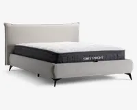 En moderne seng med en lysebeige polstret ramme og hovedgærde, udstyret med en tyk, quiltet madras med hvid top og mørkegrå sider. Madrassen har et synligt mærkenavn 'SWEETNIGHT' på siden og en blød, ekstra polstret overflade for øget komfort. Sengen står på slanke, sorte ben, hvilket giver et moderne udtryk.