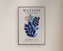 Et indrammet kunsttryk med lys træramme og cremefarvet baggrund, med markante bladlignende former i blå og mørkeblå, en lille ferskenfarvet cirkel øverst samt sort tekst med "MATISSE" og "PAPIERS DÉCOUPÉS".