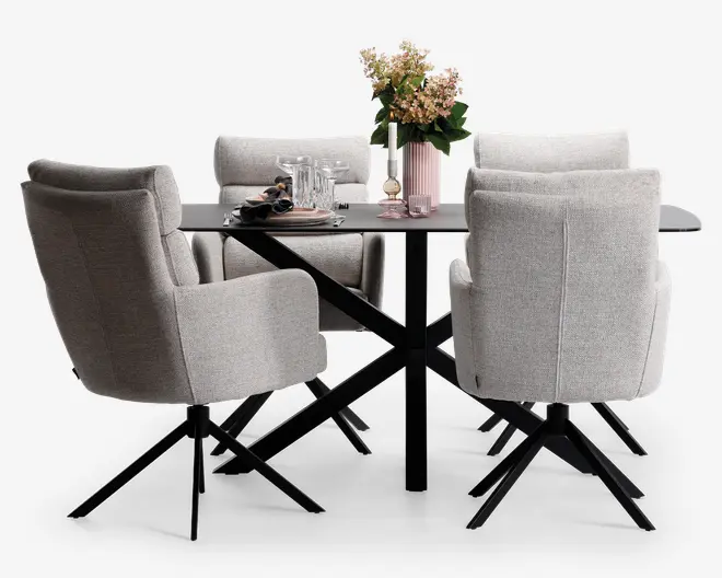 Sæt med seks polstrede spisebordsstole i lysegråt stof med blød polstring og høje rygge, placeret omkring et rektangulært sort spisebord med krydsede metalben. Bordet er pyntet med en lyserød vase med blomster, glas og service, hvilket skaber en moderne og indbydende spiseplads.