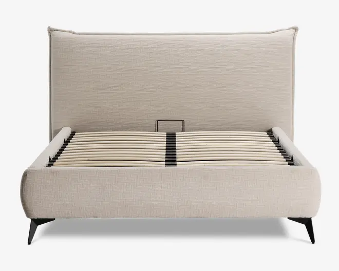 En moderne sengeramme med høj, polstret sengegavl i et lyst beige stof med diskret tekstur. Rammen har afrundede kanter og lav profil, med buede trælameller til madrasstøtte. Benene er skrå og lavet af mørkt træ eller metal, hvilket giver et solidt fundament og et moderne udtryk.