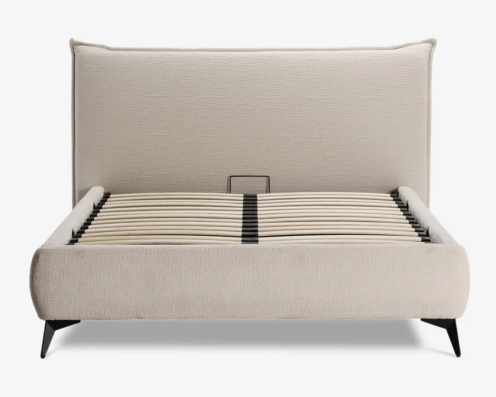 En moderne sengeramme med høj, polstret sengegavl i et lyst beige stof med diskret tekstur. Rammen har afrundede kanter og lav profil, med buede trælameller til madrasstøtte. Benene er skrå og lavet af mørkt træ eller metal, hvilket giver et solidt fundament og et moderne udtryk.