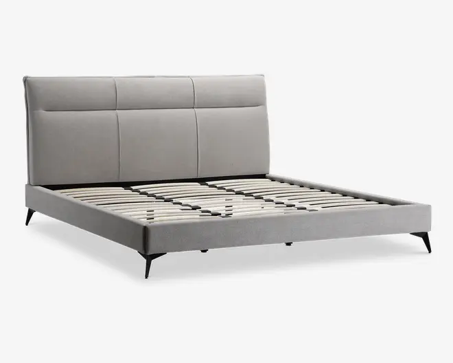 Moderne sengegavl med lysegråt polstret hovedgærde, der har tre lodrette paneler. Rammen har samme grå stofbetræk og står på slanke, skråtstillede sorte ben. Bundrammen består af jævnt fordelte trælameller til madrasstøtte, uden madras inkluderet.