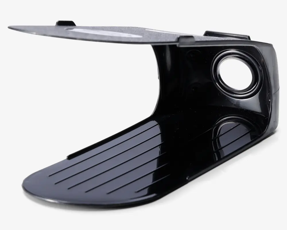 Sort plastkomponent med buet, rillet bund og flad topsektion. Toppen har en metallisk overflade og et cirkulært hul forstærket med en metalring, sandsynligvis til montering eller fastgørelse. Designet har rene linjer og en blank overflade, hvilket tyder på holdbarhed og nem rengøring.