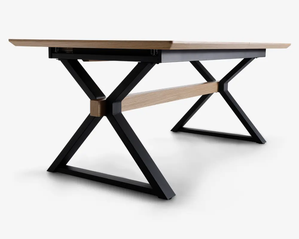 Rektangulært bord med en lys træbordplade og sorte metalben i X-form. Bordet har en matchende lys træstang, der forbinder benene for ekstra stabilitet. Designet er moderne og industrielt med rene linjer og solid konstruktion.