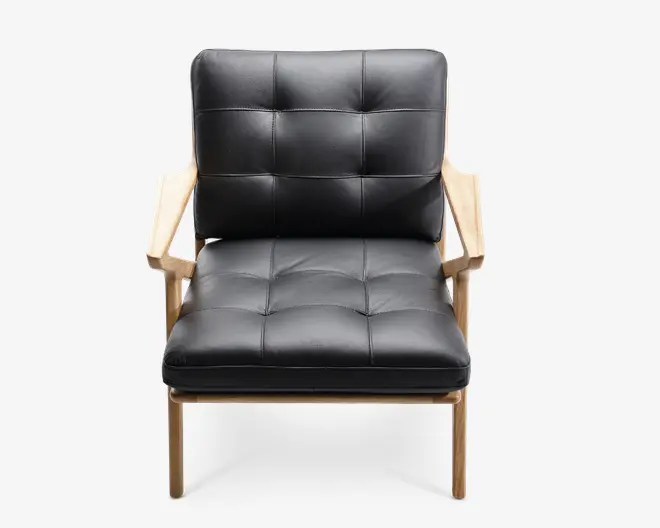 Stol med polstret sæde og ryglæn betrukket med sort kunstlæder, der har et kvadratisk, knapstukket mønster. Stellet og armlænene er lavet af lyst træ, hvilket giver et moderne og minimalistisk udtryk. Sæde- og rygpuderne virker tykke og støttende, og armlænene er flade og brede for ekstra komfort.