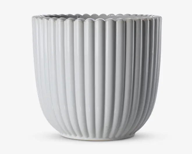 En blank, hvid keramisk beholder med lodrette riller og bølget kant. Designet er moderne og minimalistisk med jævnt fordelte riller, der løber fra bunden til toppen og giver et stilfuldt og elegant udtryk.