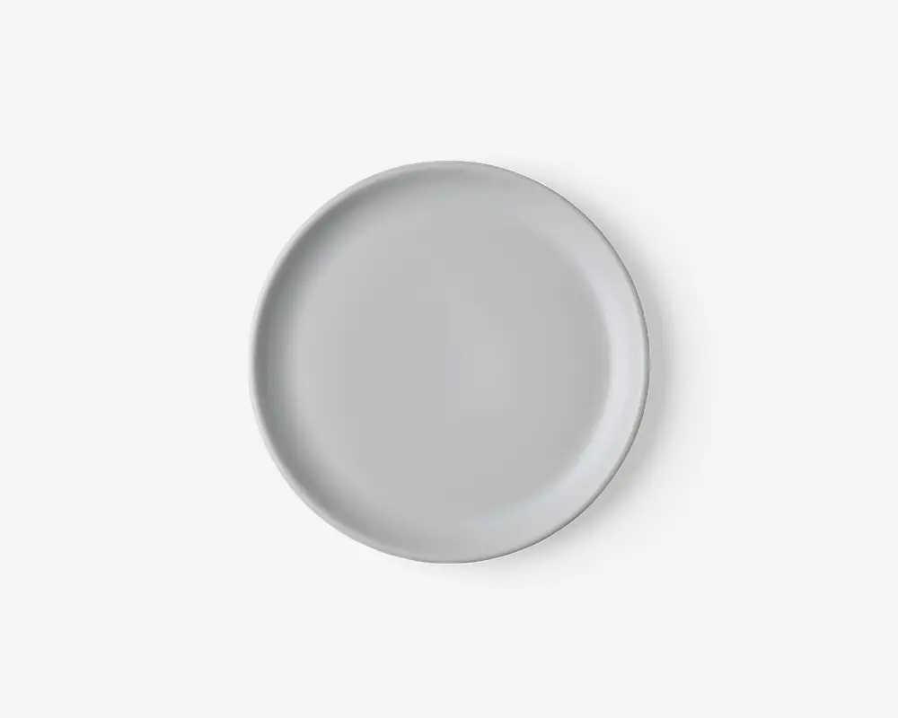 En rund, ensfarvet hvid tallerken med en glat, blank overflade og en let hævet kant. Designet er minimalistisk og moderne, velegnet til både hverdagsbrug og formelle middage.