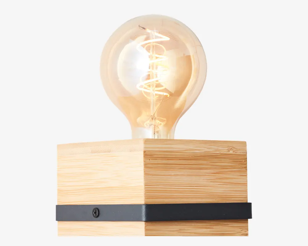 En dekorativ lampe med en stor, rund, klar glødepære, hvor den spiralformede glødetråd er synlig. Pæren er monteret på en kvadratisk træbase med naturfinish og har et vandret sort metalbånd nederst. Designet kombinerer moderne og rustikke elementer og passer godt til nutidige indretninger.