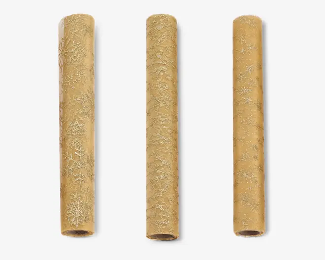 Tre cylindriske ruller brunt kraft gavepapir, hver med et diskret, gentagende mønster af hvide snefnug. Papiret har en mat overflade, og snefnugdesignene varierer i størrelse og stil, hvilket giver et festligt og elegant udtryk, der egner sig til gaveindpakning i juletiden.