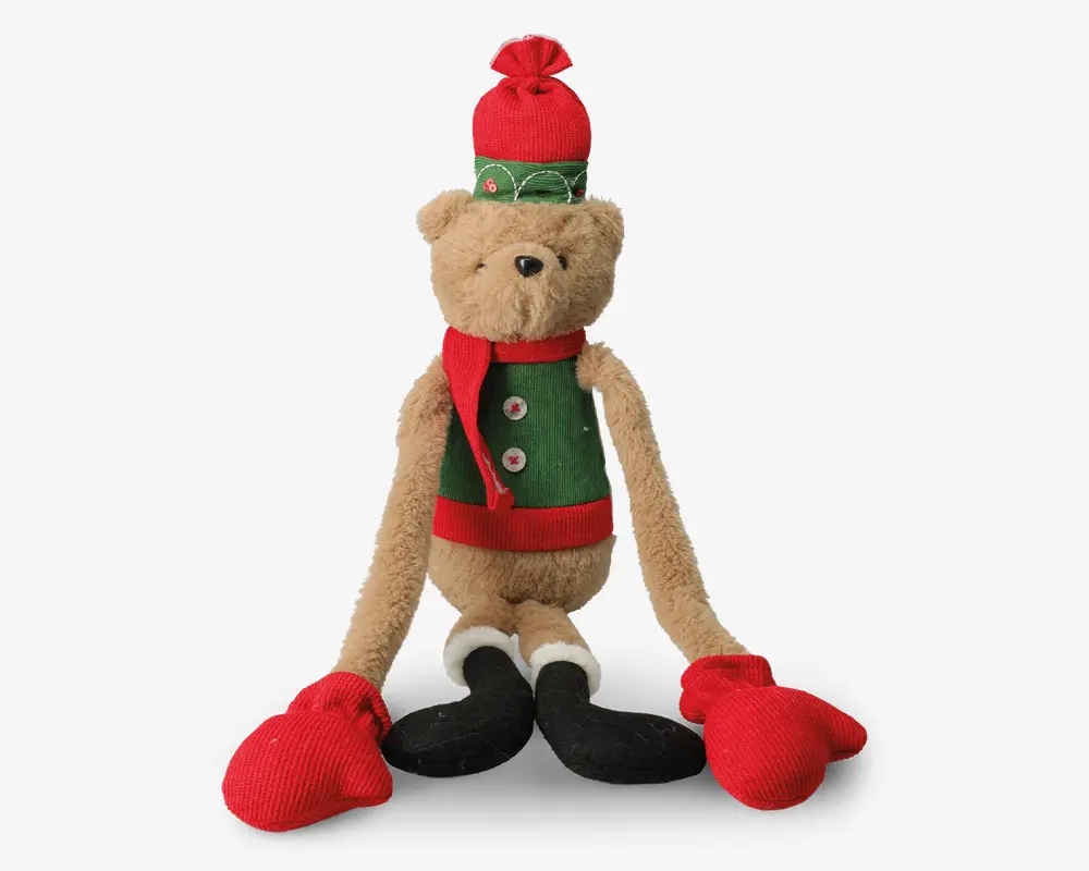 Bamse med lysebrun pels, iført grøn vest med rød kant og hvide knapper, rød halstørklæde, rød og grøn vinterhue med kvast samt store røde vanter og sorte støvler. Bamsen har lange arme og ben, hvilket giver den et sjovt og festligt udtryk.