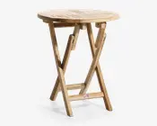 Rundt bord i træ med lamelbordplade og naturfinish. Bordet har et sammenklappeligt design med krydsede ben og en støttebjælke for stabilitet. Træets årer er synlige, hvilket giver et rustikt og afslappet udtryk, velegnet til både indendørs og udendørs brug.