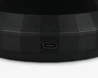 Nærbillede af en sort, tekstureret overflade med en USB-C opladningsport. Over porten er teksten '5V⎓1A' indgraveret, hvilket angiver strømindgangens specifikationer. Overfladen har et facetformet, geometrisk design.