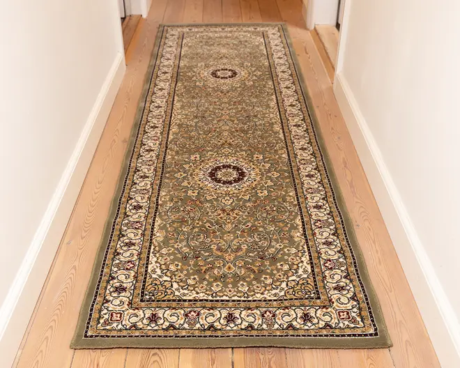 Lang, rektangulær løber med et indviklet blomster- og medaljonmønster i dæmpede grønne, beige og bordeaux nuancer. Tæppet har en detaljeret kant med snoede motiver og små blomsterdetaljer, og midterområdet viser to cirkulære medaljoner. Luvet ser lav ud, og kanterne er pænt afsluttet.