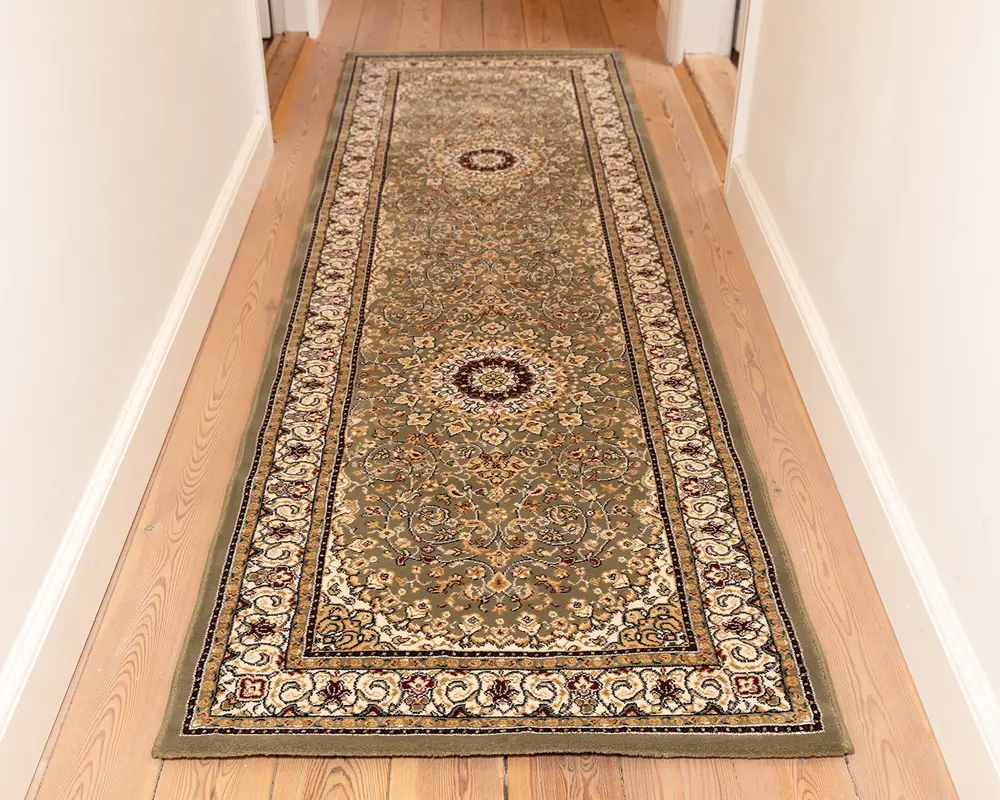 Lang, rektangulær løber med et indviklet blomster- og medaljonmønster i dæmpede grønne, beige og bordeaux nuancer. Tæppet har en detaljeret kant med snoede motiver og små blomsterdetaljer, og midterområdet viser to cirkulære medaljoner. Luvet ser lav ud, og kanterne er pænt afsluttet.