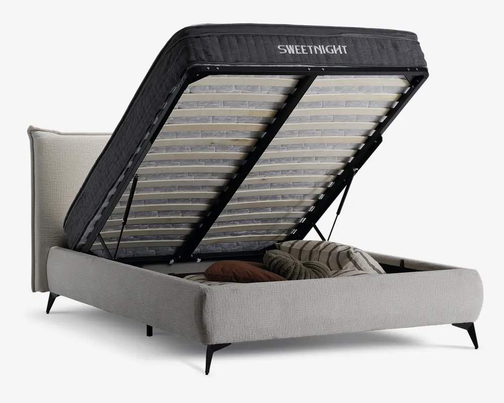 Polstret senge ramme med løftbar lamelbund, der afslører et rummeligt opbevaringsrum under sengen. Opbevaringsområdet indeholder puder og sengetøj. Sengen har et lyst stofbetræk og sorte ben, og madrassens støtte er hævet for nem adgang.