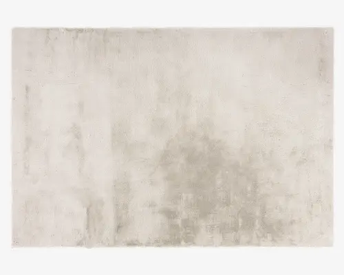 Rektangulært tæppe med en blød, plysset tekstur og en ensartet lys beige farve. Overfladen har et diskret, let meleret udseende, hvilket giver et moderne og elegant præg. Kanterne er pænt afsluttede, og luven virker tæt og behagelig at gå på.