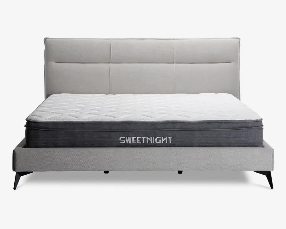 En moderne seng med et lysegråt polstret hovedgærde og ramme, udstyret med en tyk madras med quiltet hvid top og mørkegrå sider. Madrassen har mærket 'SWEETNIGHT' broderet på siden. Hovedgærdet har et stilrent, panelopdelt design, og sengen står på korte, skråtstillede sorte ben.