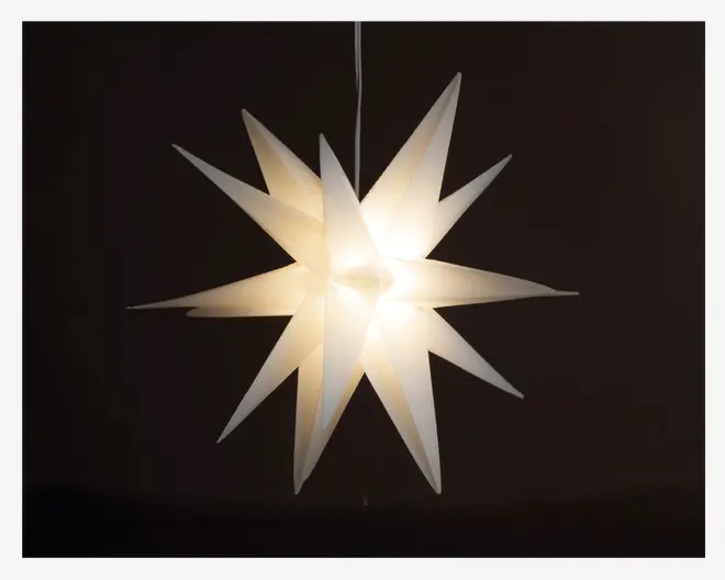Hængende lampe med tredimensionel stjerneform, der har flere aflange spidser, som stråler ud fra midten. Materialet virker gennemsigtigt og lader et blødt, varmt lys skinne igennem. Designet er moderne og dekorativt, velegnet til festlig eller stemningsfuld belysning.