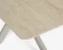 Nærbillede af en lys beige bordplade med diskret stenlignende struktur, afrundet hjørne og slanke hvide skrå ben.