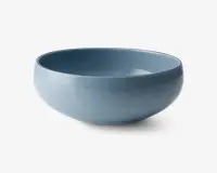 Rund skål med en glat, blank overflade i en afdæmpet blå farve. Skålen har et enkelt, moderne design med blødt buede sider og en let tyk kant. Både indersiden og ydersiden er ensfarvet, og skålen ser ud til at være lavet af keramik eller porcelæn.