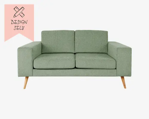 En moderne to-personers sofa med dæmpet grøn stofpolstring. Sofaen har et enkelt, lige design med brede, rektangulære armlæn og to separate sæde- og ryghynder for ekstra komfort. Benene er skråtstillede og lavet af lyst træ, hvilket giver sofaen et moderne og let skandinavisk udtryk.