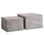 Sæt med to kubeformede borde lavet af grå marmor med naturlige årer. Bordene har en glat, poleret overflade og et minimalistisk, blokagtigt design. Det ene bord er lidt højere og større end det andet, så de kan placeres sammen eller ved siden af hinanden. Marmormønsteret varierer på hver flade, hvilket giver et unikt og elegant udtryk.