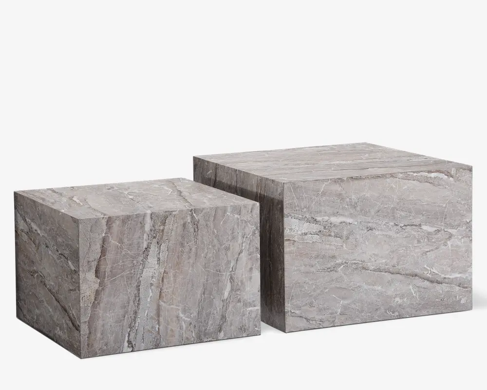 Sæt med to kubeformede borde lavet af grå marmor med naturlige årer. Bordene har en glat, poleret overflade og et minimalistisk, blokagtigt design. Det ene bord er lidt højere og større end det andet, så de kan placeres sammen eller ved siden af hinanden. Marmormønsteret varierer på hver flade, hvilket giver et unikt og elegant udtryk.