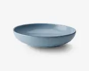 En rund, lav skål med en glat mat blå yderside og en blank blå inderside. Skålens kant er let hævet og har en diskret mørk kant, hvilket giver skålen et moderne og elegant udtryk.