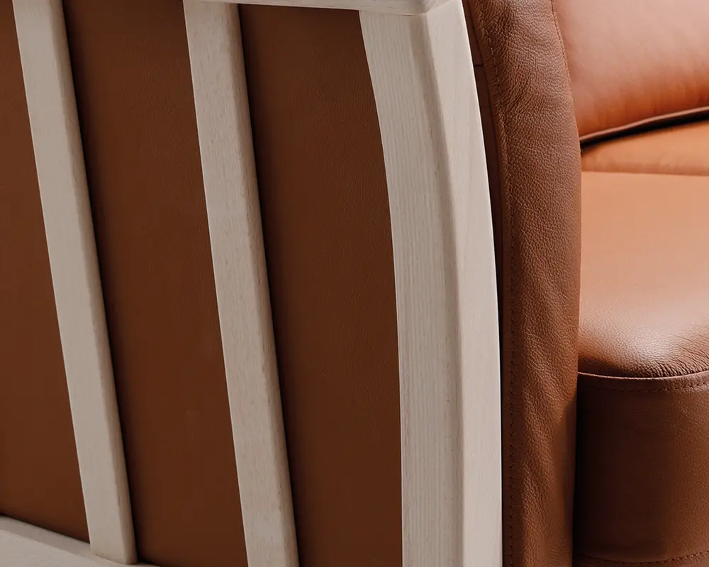 Nærbillede af et møbel med glat, lysebrunt læderbetræk og en ramme af lyst træ. Læderet ser blødt og velpolstret ud med synlige syninger langs kanterne. Trærammen har en naturlig finish og lodrette lameller, hvilket giver et moderne og solidt udtryk.