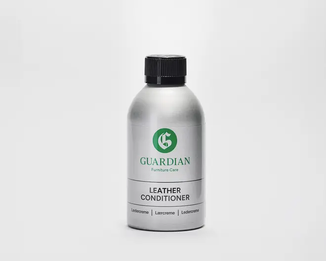 En sølvfarvet flaske med sort skruelåg, hvor mærket 'Guardian' og produktnavnet 'Leather Conditioner' er trykt på forsiden med grøn og sort tekst. Flasken har et enkelt, moderne design med tydelig mærkning, og teksten er præsenteret på flere sprog. Beholderen ser ud til at være lavet af metal eller metallisk plast, hvilket giver et indtryk af holdbarhed og kvalitet.