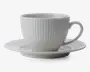 En hvid keramikkop med tilhørende underkop, begge med lodrette riller i overfladen. Koppen har en rund form med et behageligt håndtag, og underkoppen har en let forhøjet kant. Designet er minimalistisk og elegant.