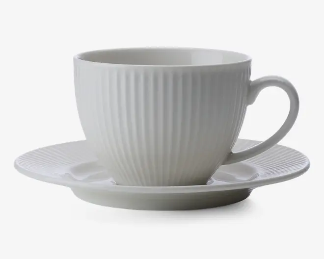 En hvid keramikkop med tilhørende underkop, begge med lodrette riller i overfladen. Koppen har en rund form med et behageligt håndtag, og underkoppen har en let forhøjet kant. Designet er minimalistisk og elegant.