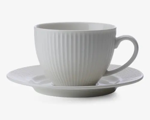 En hvid keramikkop med tilhørende underkop, begge med lodrette riller i overfladen. Koppen har en rund form med et behageligt håndtag, og underkoppen har en let forhøjet kant. Designet er minimalistisk og elegant.
