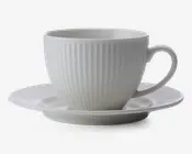 En hvid keramikkop med tilhørende underkop, begge med lodrette riller i overfladen. Koppen har en rund form med et behageligt håndtag, og underkoppen har en let forhøjet kant. Designet er minimalistisk og elegant.