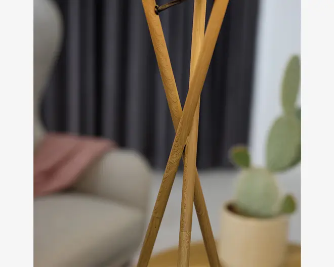 Tre slanke, lyse træstænger krydser hinanden og står oprejst, hvilket danner en tripod-struktur. Træet har en glat, naturlig finish med synlige åremønstre. Toppen af stængerne er samlet med en lille metalforbindelse. Designet er minimalistisk og moderne, velegnet til nutidige indretninger.