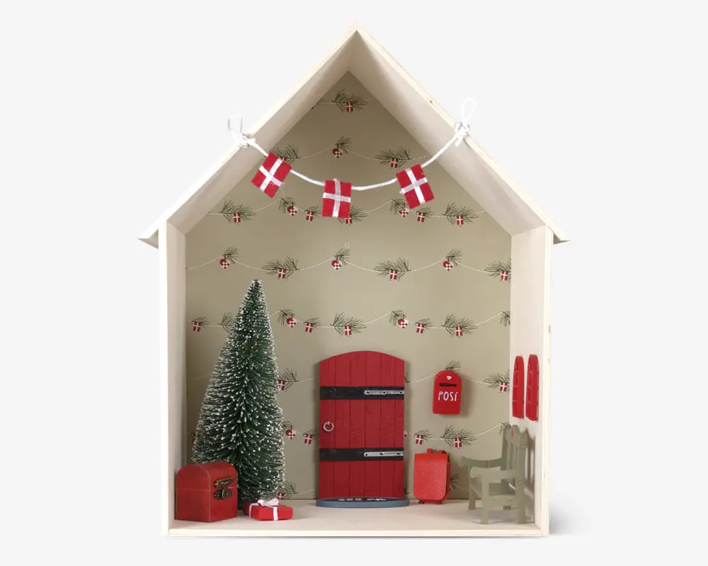 Miniature julescene i et husformet træramme. Indeholder en lille rød dør med sorte hængsler, et grønt grantræ med hvide sne-detaljer, en rød postkasse med teksten 'post', en grøn bænk, røde ski monteret på væggen, en rød kiste og en lille indpakket gave. Baggrunden er dekoreret med en guirlande af dannebrogsflag og grangrene.