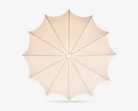 Set ovenfra af en stor, rund udendørs parasol med beige stofdug. Dugen er opdelt i tolv sektioner af jævnt fordelte støtteben, hvilket skaber et symmetrisk, stjernelignende mønster. Stoffet er stramt spændt ud, og kanten har en let bølget, dekorativ finish.