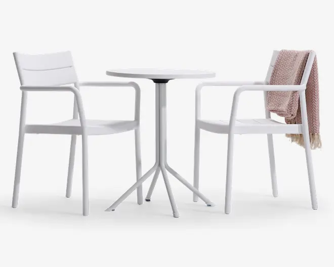 Sættet består af to hvide stole med armlæn og et matchende rundt bord. Stolene har et moderne, minimalistisk design med let buede ryg- og sædeflader. På den ene stol hænger et tekstureret, lysebrunt tæppe over ryglænet. Bordet har en slank, rund bordplade og en solid base med fire ben.