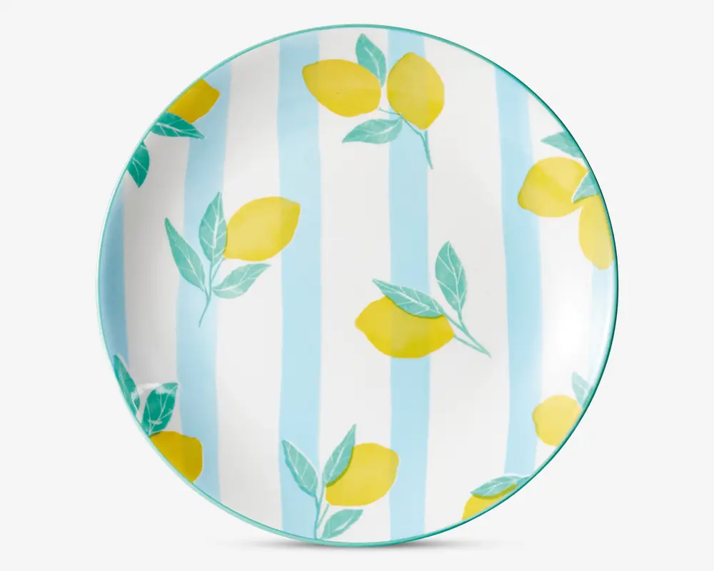 Rund tallerken med et mønster af lysegule citroner med grønne blade, placeret på en baggrund med skiftevis lyseblå og hvide lodrette striber. Tallerkenens kant er markeret med en tynd turkis linje.