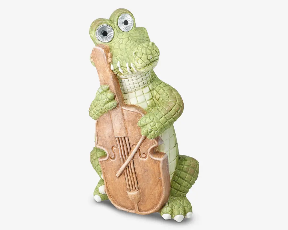 En finurlig figur af en grøn krokodille med teksturerede skæl og store, tegneserieagtige øjne, der holder en brun cello. Krokodillen har et venligt udtryk og er poseret, som om den spiller på instrumentet, med den ene hånd på halsen og den anden på cellokroppen. Figuren har detaljeret udformning både på krokodillen og celloen, hvilket giver den et legende og charmerende udseende.